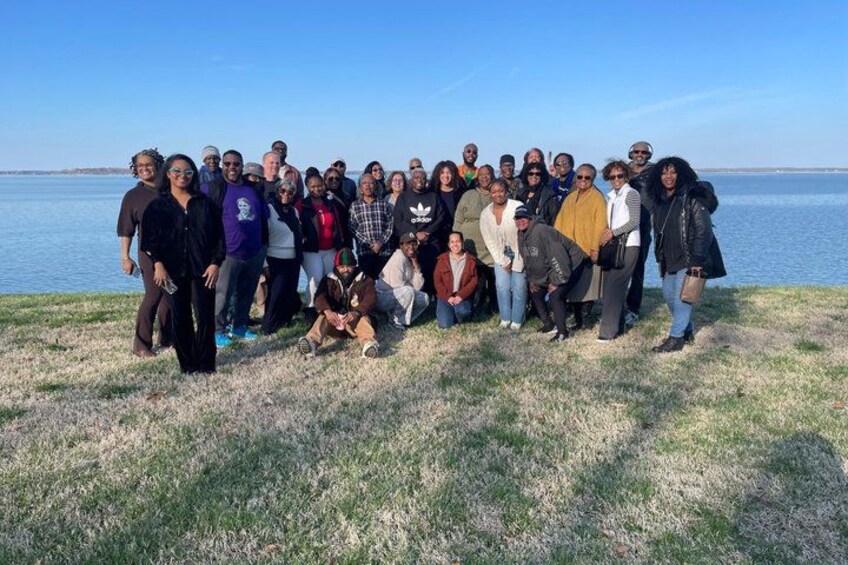 A group of people standing on a grassy area by a body of water. 2