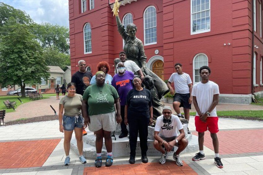 A group of people posing in front of a statue and a red building. 4