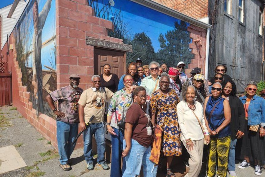 A group of people standing in front of a mural on a brick wall. 5