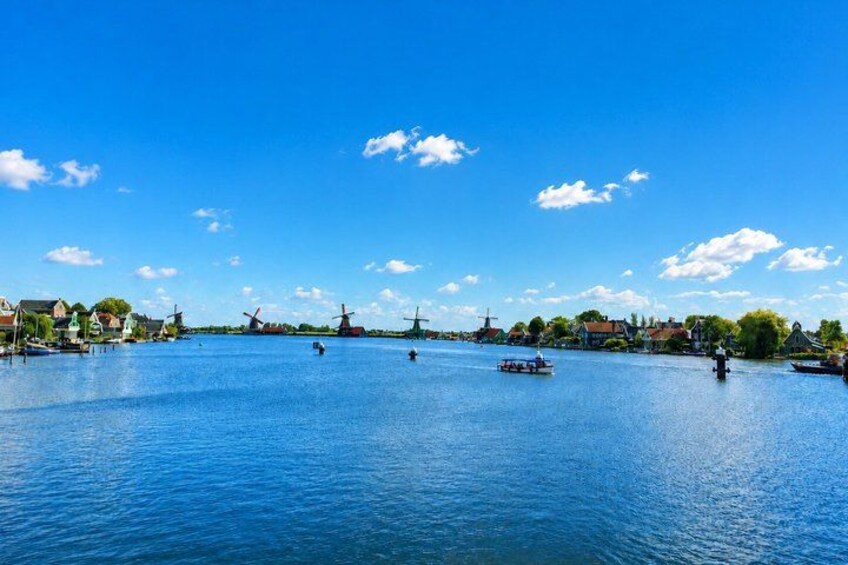 A calm river with windmills and boats, surrounded by houses and greenery. 3
