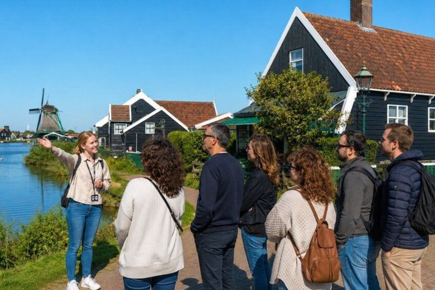 A group of people standing by a canal with traditional houses and a windmill in the background. 5