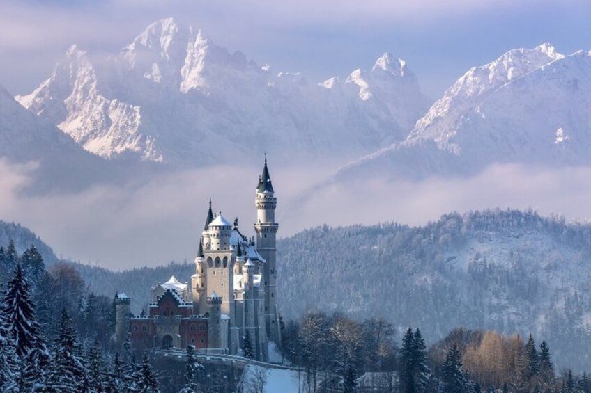 A snow-covered castle with multiple towers, surrounded by a forest and mountains in the background. 5