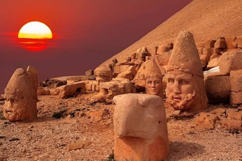 Ancient stone heads and a pyramid in the desert at sunset. 1