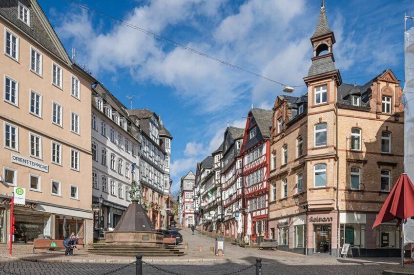A European street with historic buildings, a fountain, and a clear blue sky. 4