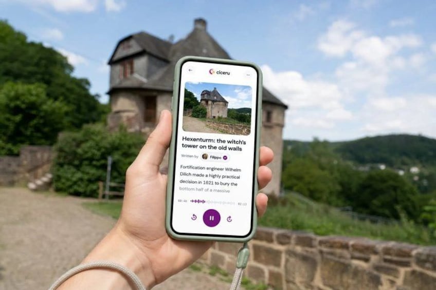 A hand holding a smartphone displaying a castle with a caption about Hexenturm. 1
