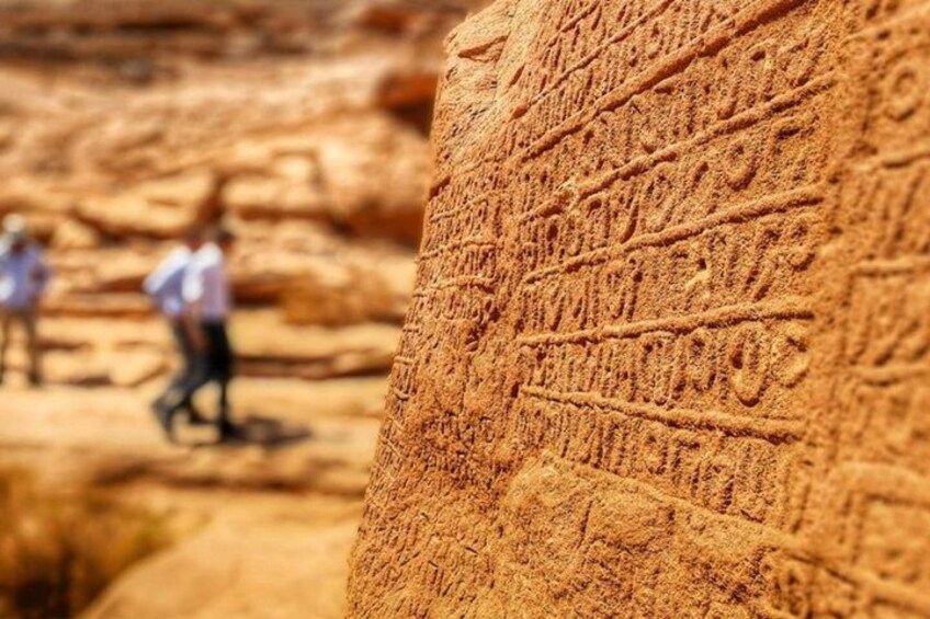 A close-up of ancient carvings on a sandstone rock with people in the background. 1