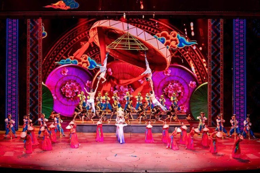 A stage with performers in colorful costumes, a large circular backdrop, and a central figure suspended above the stage. 3
