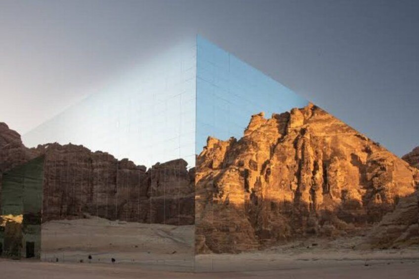 A desert landscape with a prominent rock formation and a modern glass building. 4