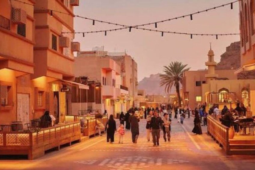 A bustling street with people walking, buildings with balconies, and a palm tree in the background. 1