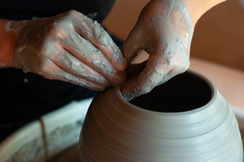 Hands shaping a clay pot on a wheel. 2