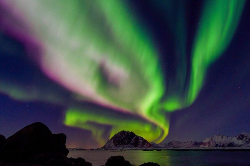 The Northern Lights over a mountainous landscape with a body of water. 1
