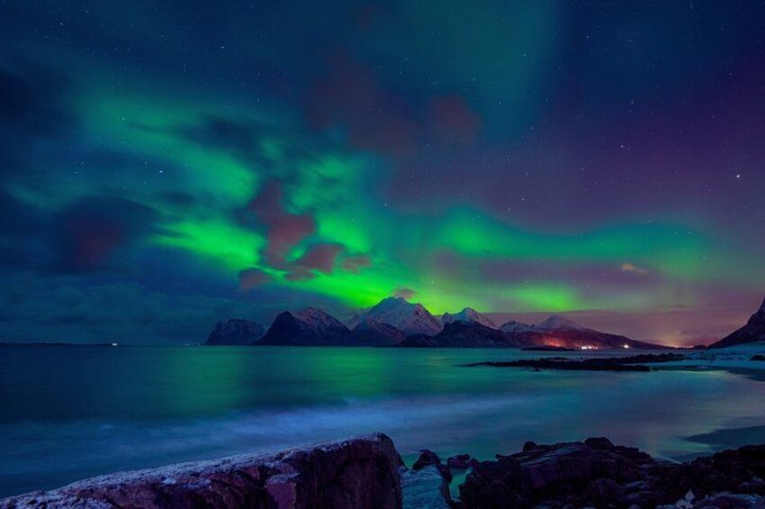 A night scene with the Northern Lights over a mountainous landscape and a calm body of water. 4