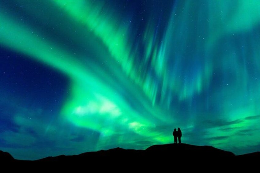 A night sky with green aurora borealis over a silhouette of a person standing on a hill. 3