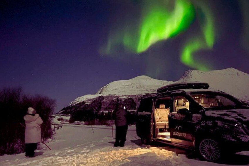 A snow-covered landscape with a vehicle and people observing the Northern Lights. 2