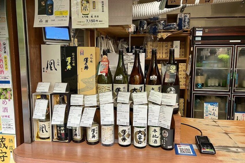 A variety of sake bottles and boxes on display with price tags. 2