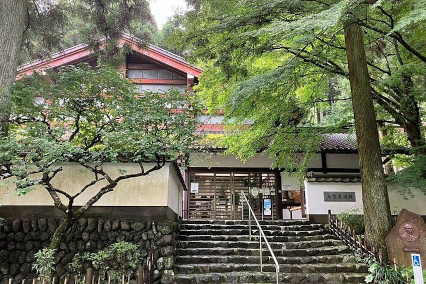 A traditional Japanese temple with stone steps leading up to a red-roofed building, surrounded by lush greenery. 5