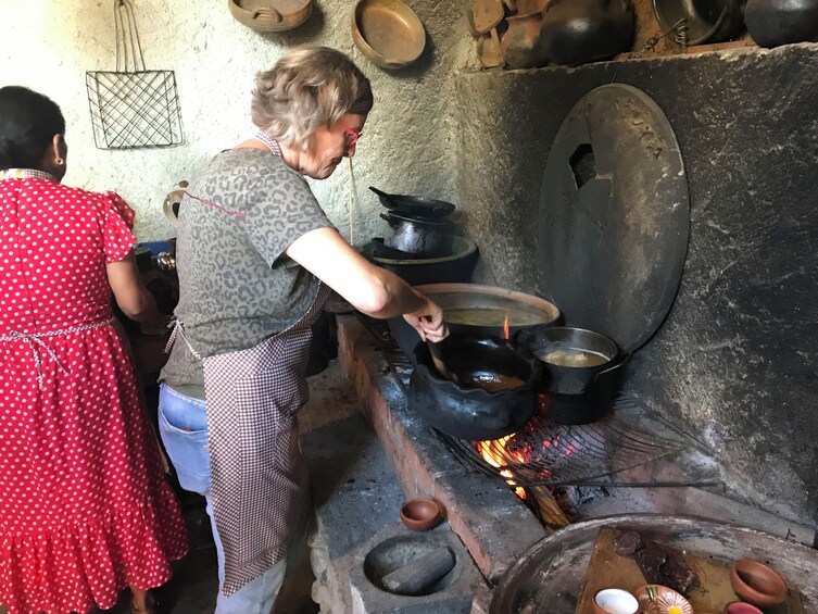 A woman cooking over an open fire in a traditional kitchen with pots and pans. 3