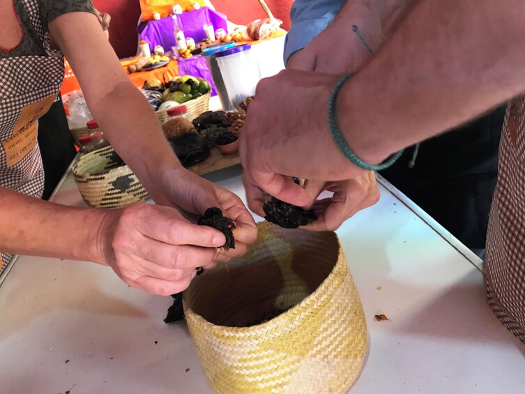 Hands holding a dark object over a woven basket. 4
