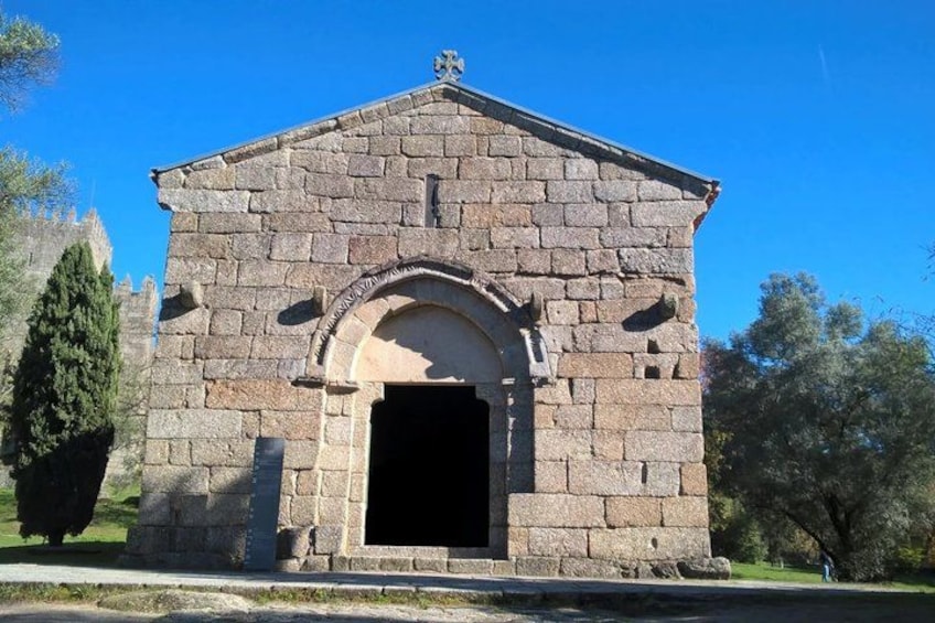 A stone building with a central archway, surrounded by trees and a clear blue sky. 1