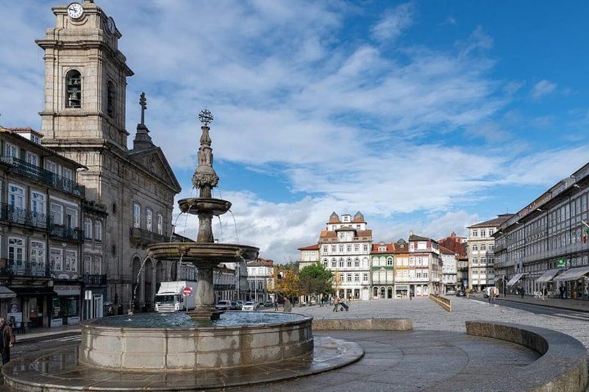 A historic square with a fountain, a clock tower, and classical architecture. 2