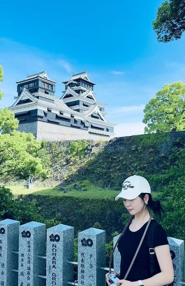 A person standing in front of a traditional Japanese castle with multiple tiers and a stone monument with inscriptions. 4