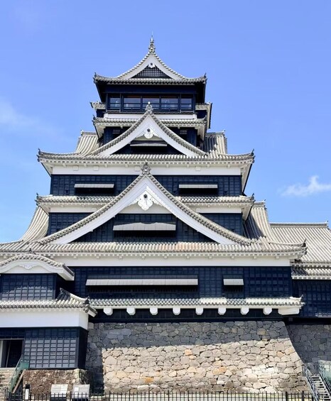 A traditional Japanese castle with multiple tiers, stone walls, and a clear blue sky in the background. 3