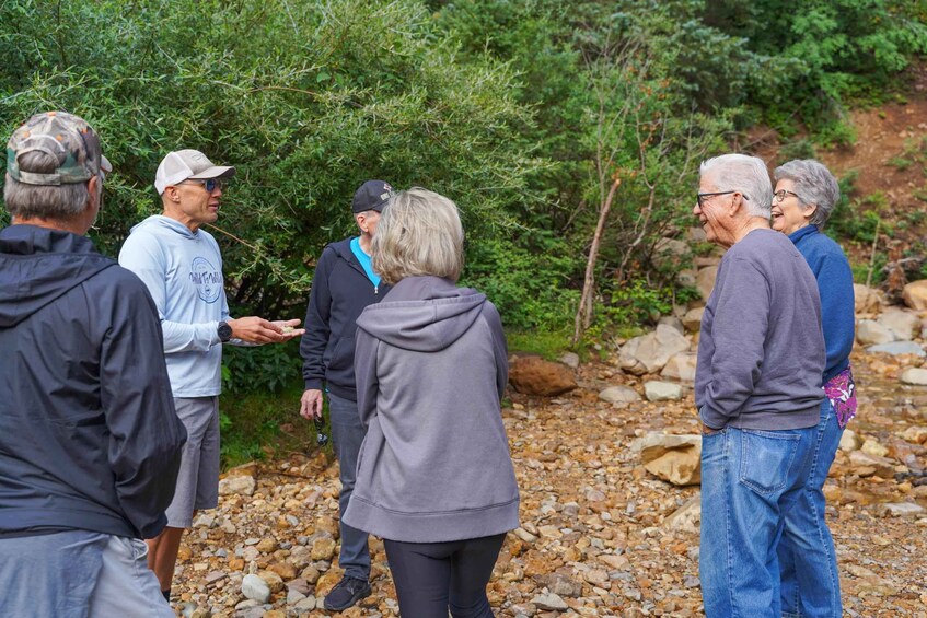 A group of people standing outdoors near a rocky stream with greenery in the background. 1
