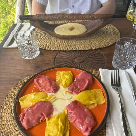 Une assiette de raviolis nappés d'une sauce à base de tomates, une planche en bois servant de plat avec une tranche de pain, et deux verres d'eau sur une table. 3