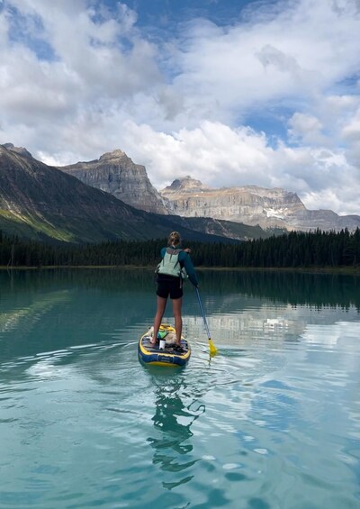 A person paddleboarding on a calm lake with mountains in the background. 3