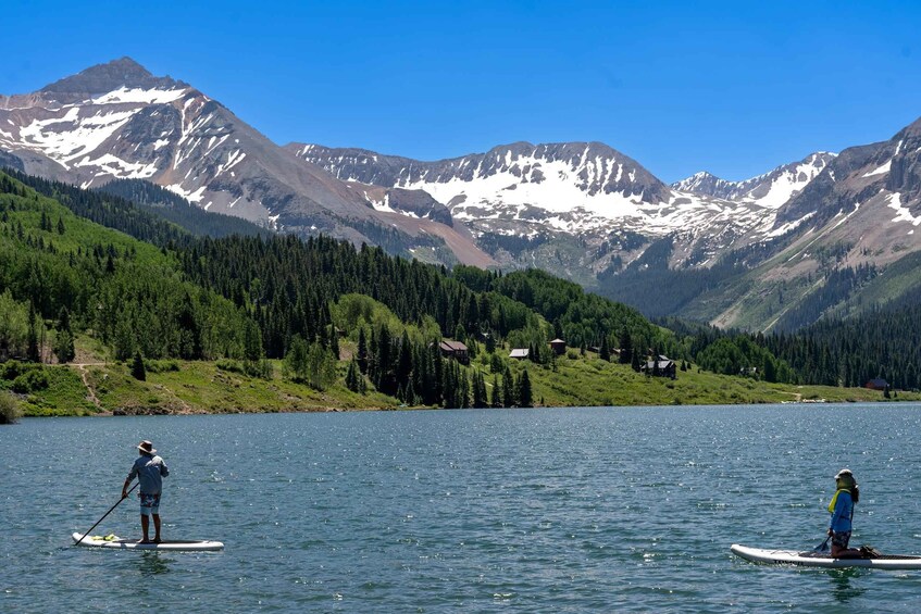 Two people paddleboarding on a calm lake with mountains in the background. 1