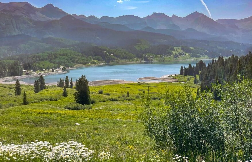 A mountainous landscape with a lake, green fields, and coniferous trees. 2