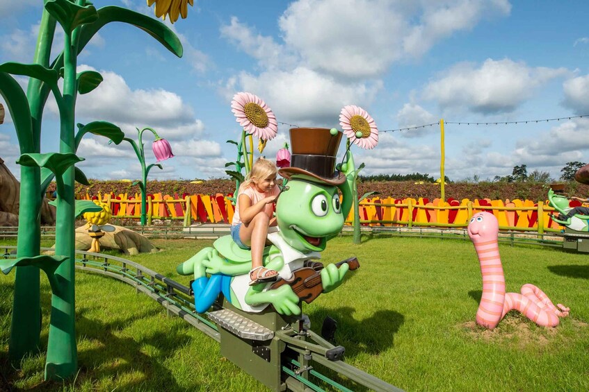 A child riding a green caterpillar on a track, surrounded by oversized flowers and a caterpillar sculpture. 5