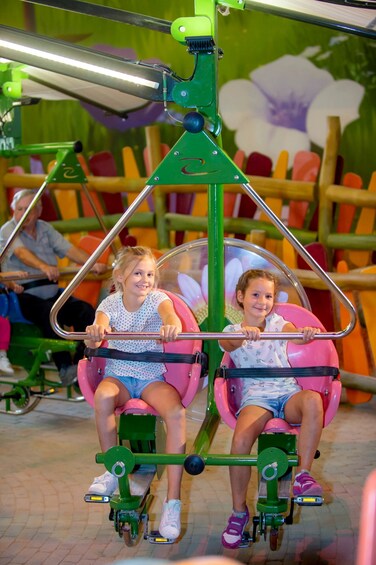Two children seated on a green and pink amusement ride with a metal frame. 3