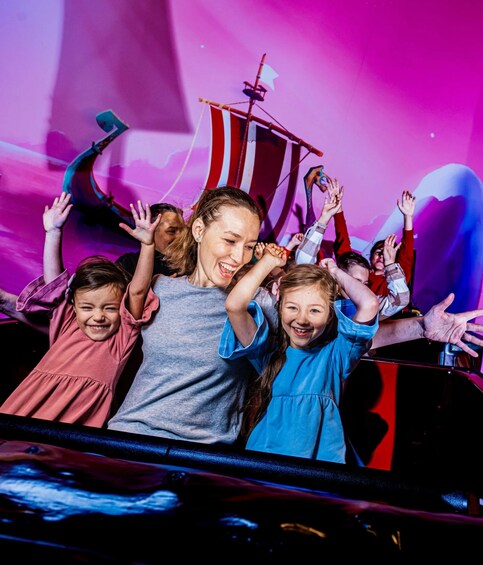 A group of people on a ride with a ship and flag in the background. 1