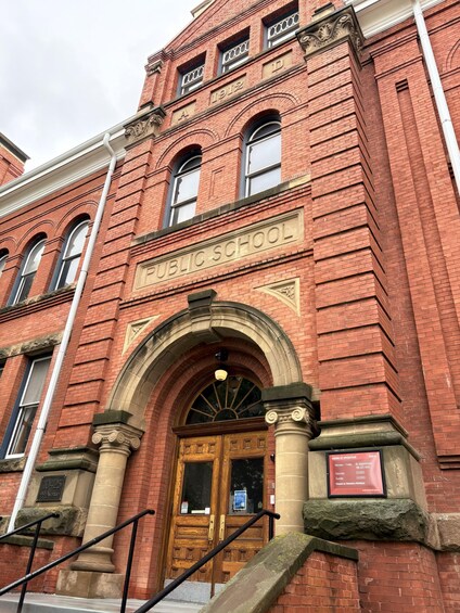 A red brick public school building with a large arched entrance and a wooden door. 2