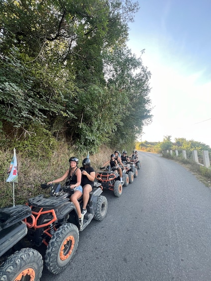 A group of people riding atv's on a road surrounded by trees. 2