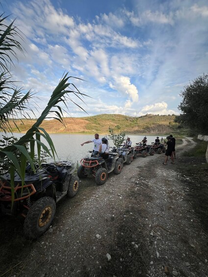 A group of people on ATVs by a lake with a hilly landscape in the background. 1