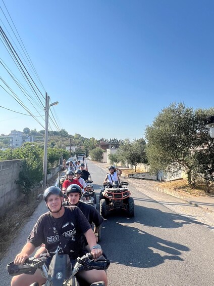 A group of people on ATVs on a road with houses and trees in the background. 4