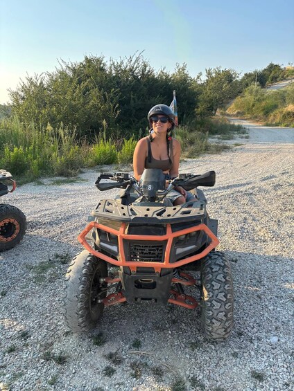 A person sitting on an ATV with a helmet and sunglasses, surrounded by gravel and greenery. 3