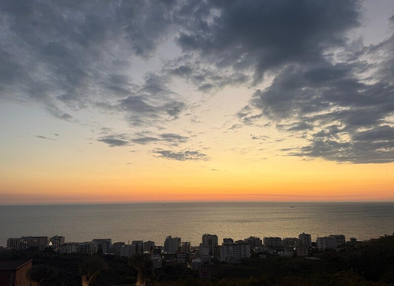 A coastal cityscape at sunset with buildings along the shore and a cloudy sky. 5