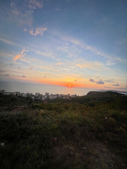 A sunset over a coastal cityscape with buildings and hills in the foreground. 3