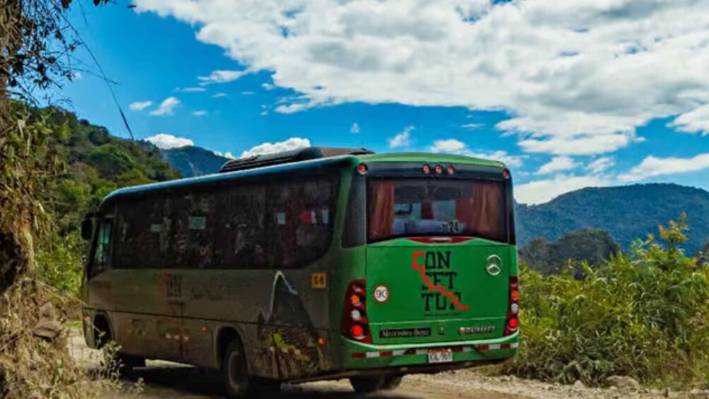Un autobus vert avec l’inscription « CONSET TUR » à l’arrière, circulant sur un chemin de terre bordé de verdure et entouré de montagnes. 3