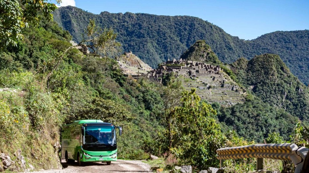 Un autobus vert sur une route de montagne, avec des champs en terrasses et un village en arrière-plan. 1
