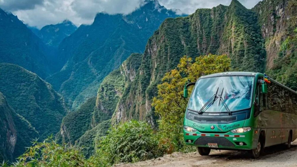 Un autobus vert est garé sur une route de montagne, avec de hautes falaises et une végétation luxuriante en arrière-plan. 2
