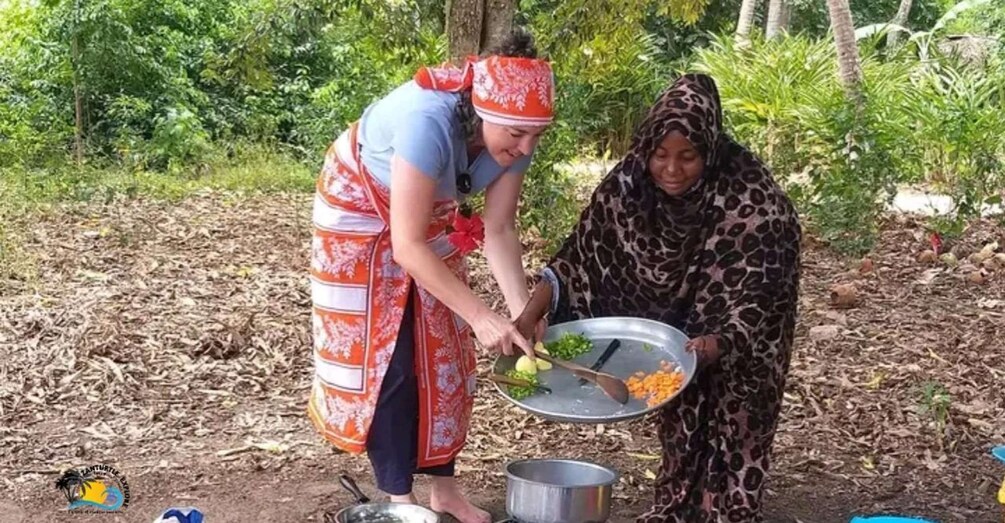 Zwei Personen bereiten im Freien Essen zu, umgeben von Bäumen und Blättern. 1