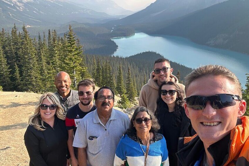 A group of people standing on a mountain overlooking a lake and forest. 5