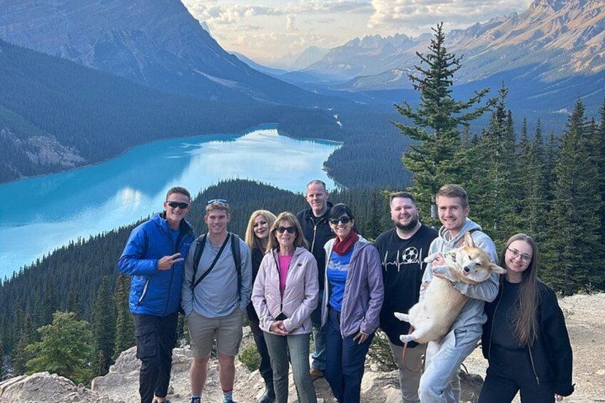 A group of people standing on a mountain with a lake and forest in the background. 5