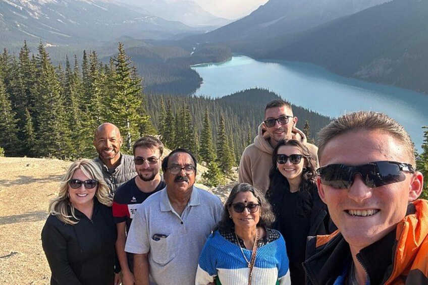 A group of people standing on a mountain overlooking a lake surrounded by trees. 4