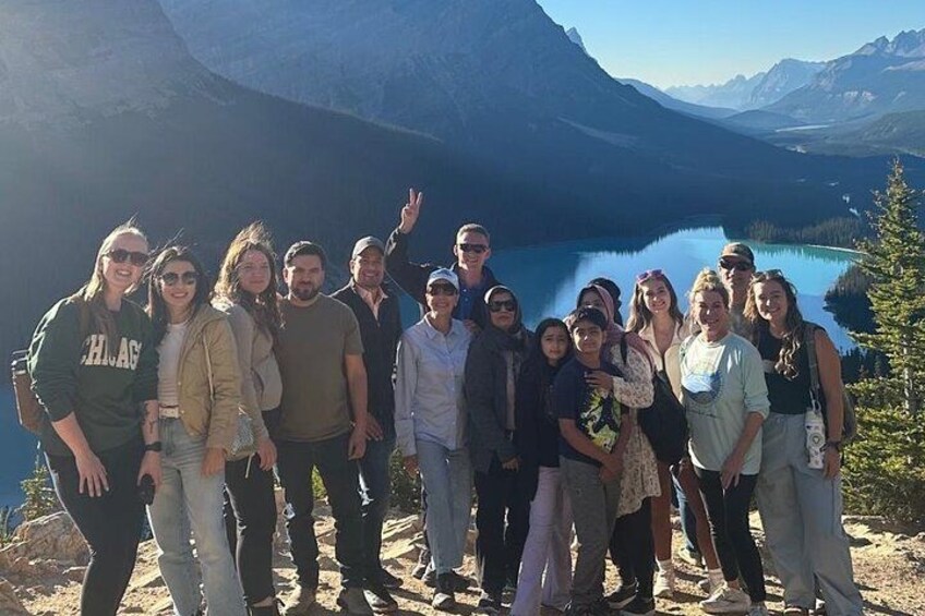 A group of people standing on a mountain overlooking a lake with mountains in the background. 3