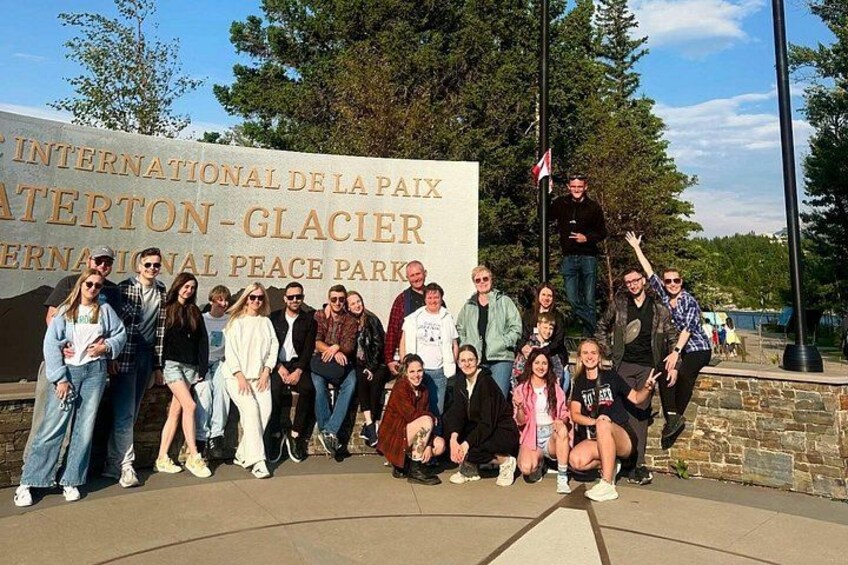 A group of people posing in front of a sign that reads 'International de la paix Glacier International Peace Park.' 4